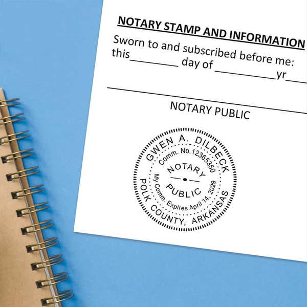 Arkansas notary seal impression on jurat form with spiral notebook on blue background.