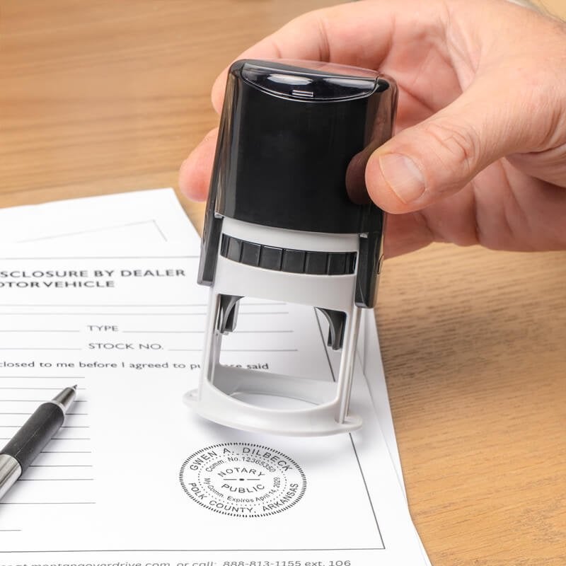 Hand stamping Arkansas notary seal on document with pen and wood desk background.