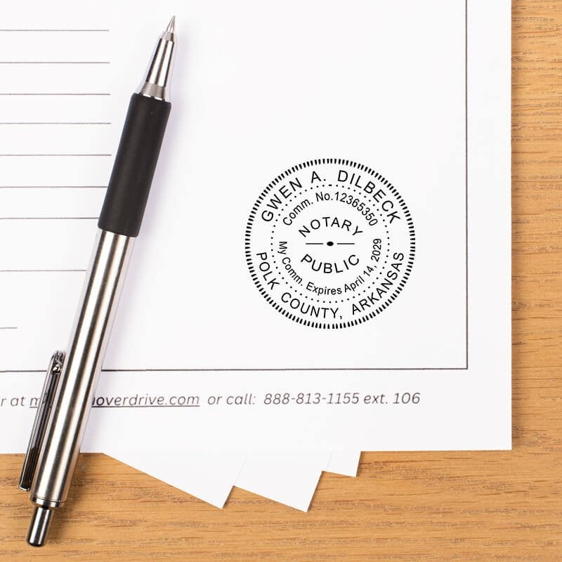 Arkansas notary stamp impression on document with striped pen on wooden desk.