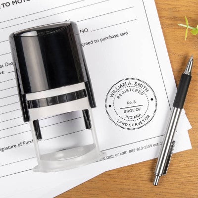 A self-inking stamp and a pen placed next to the State of Indiana Land Surveyor Seal