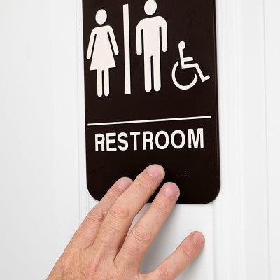 A person's hand feeling the Braille on the sign