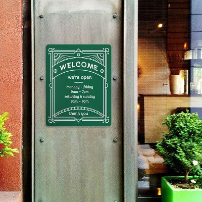 A green engraved plastic sign with a store's business hours