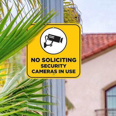 No soliciting sign with a yellow background reading Security cameras in bold hung on a pole 