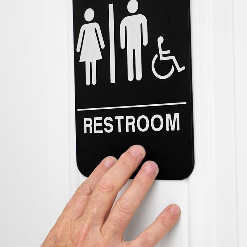 A person's hand feeling the Braille on the sign