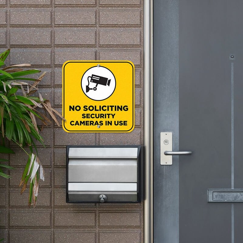 Yellow background no soliciting sign reading "security cameras in use" hung on a wall
