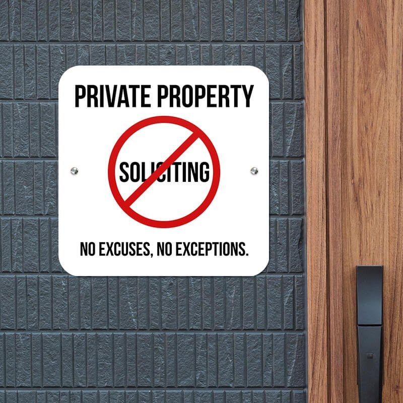 Bold Private property sign with a no soliciting symbol on a white background hung up on a gray wall.