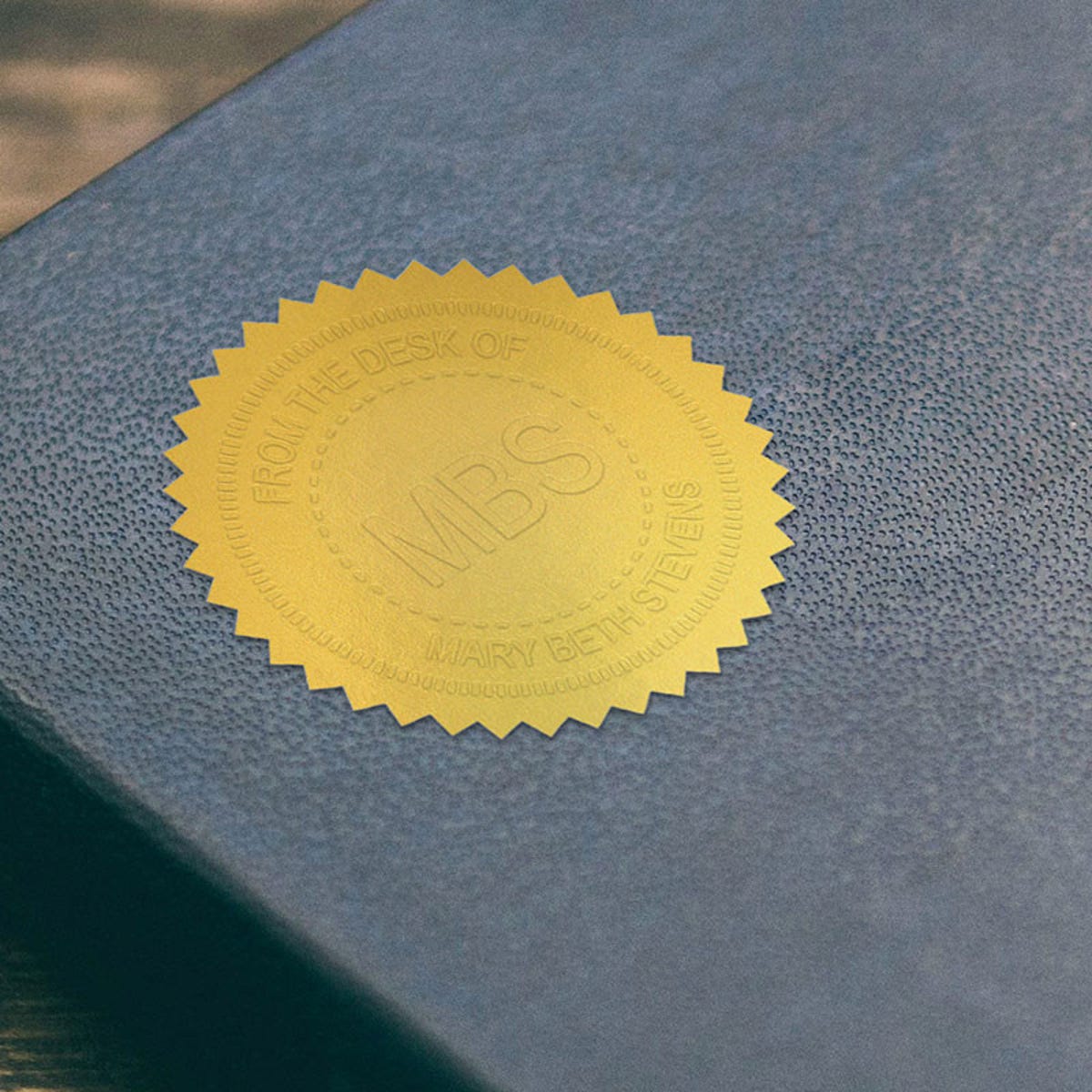 Example of Custom Initial Embosser Impression on Gold seal sticker on blue book