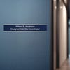 A blue name plate with a silver aluminum wall holder on an office door