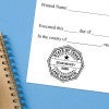 Texas notary stamp impression on white paper on a blue notebook. 