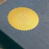 Example of the Custom Text Logo Embosser impression on gold seal on a blue book