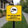 No soliciting sign with a yellow background reading Security cameras in bold hung on a pole 